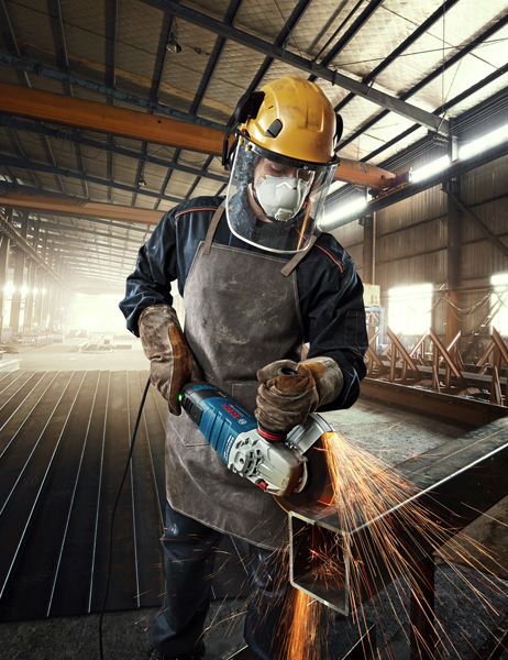A person wearing safety equipment grinds metal, producing bright sparks in a factory.