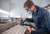 A person wearing safety equipment sands wooden planks with a random orbit sander.