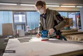 A person wearing safety equipment sands a wooden surface with a random orbit sander.