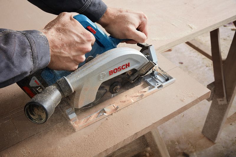 Person cutting a wooden board with a circular saw on a workbench.