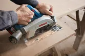 Person cutting a wooden board with a circular saw on a workbench.