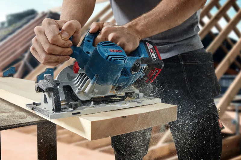 A person trims a wooden board with a circular saw, sawdust flying.