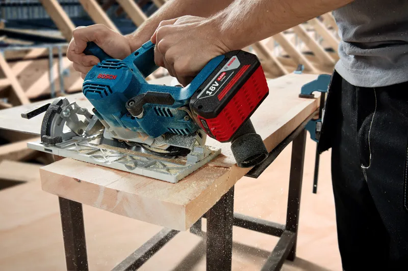 Person using a cordless circular saw to cut a wooden plank on a workbench.
