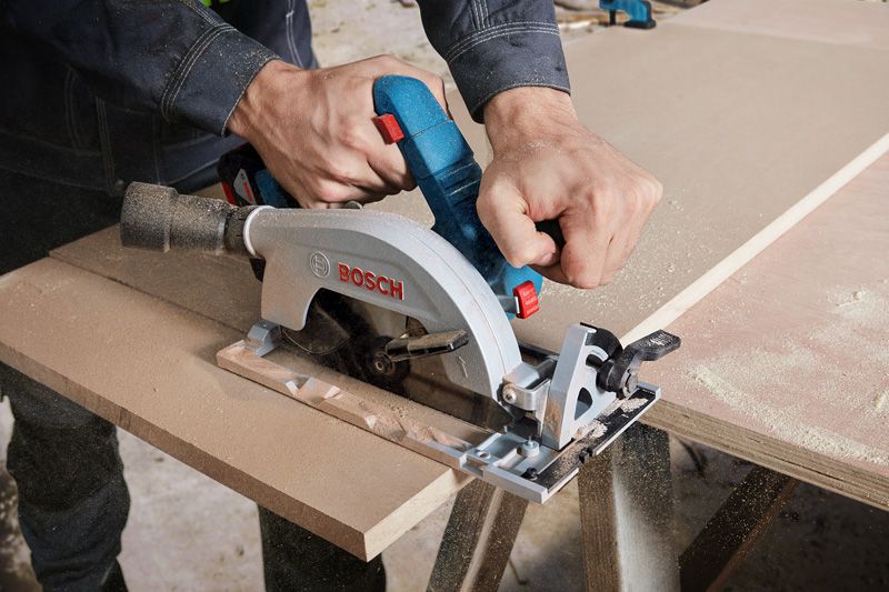 A person uses a circular saw to cut wood panels on a work table.