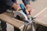 A person uses a circular saw to cut wood panels on a work table.