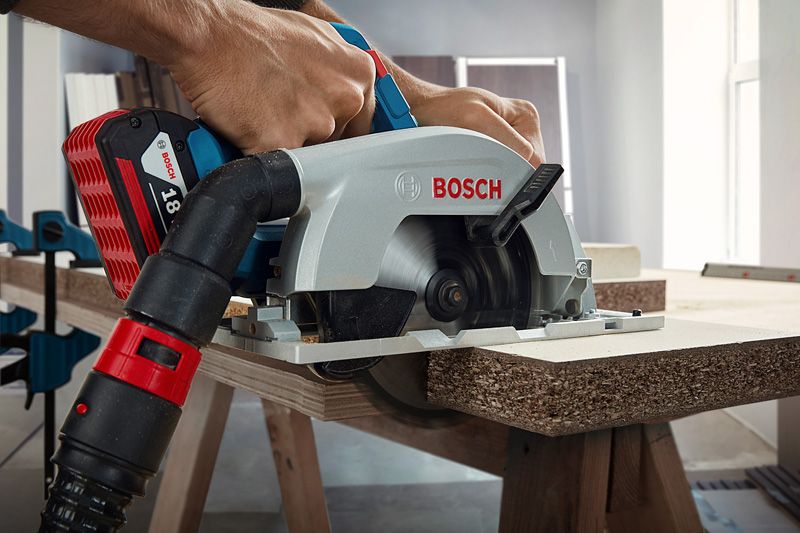 A person guides a circular saw with dust extraction while cutting chipboard.