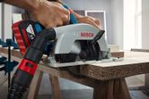 A person guides a circular saw with dust extraction while cutting chipboard.