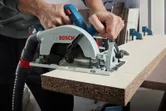 A person guides a circular saw to cut a wood board in a workshop.
