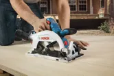 A person uses a circular saw to cut wood outdoors.