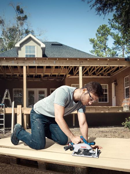 A person wearing safety equipment uses a circular saw to cut wood on a construction site.