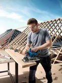 A person wearing safety equipment uses a circular saw to cut wood at a construction site.