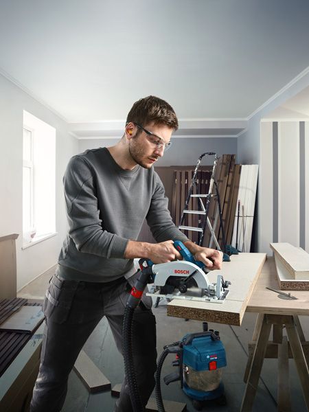 A person wearing safety equipment uses a circular saw to cut a wooden board.
