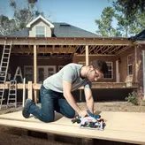 A person wearing safety equipment uses a circular saw to cut wood on a construction site.