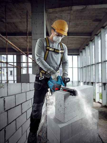 A person wearing safety equipment cuts an AAC block with a power cutter in a building under construction.