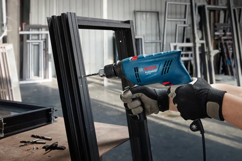 A person wearing safety equipment drills into a metal frame using an impact drill.