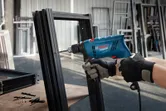A person wearing safety equipment drills into a metal frame using an impact drill.
