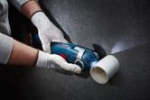 A person wearing safety equipment cuts a plastic pipe with a cordless oscillating tool.
