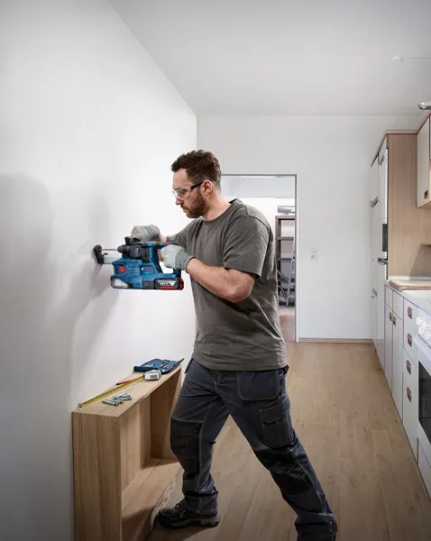 Person wearing safety equipment drills into a wall near a measuring tool and screws.