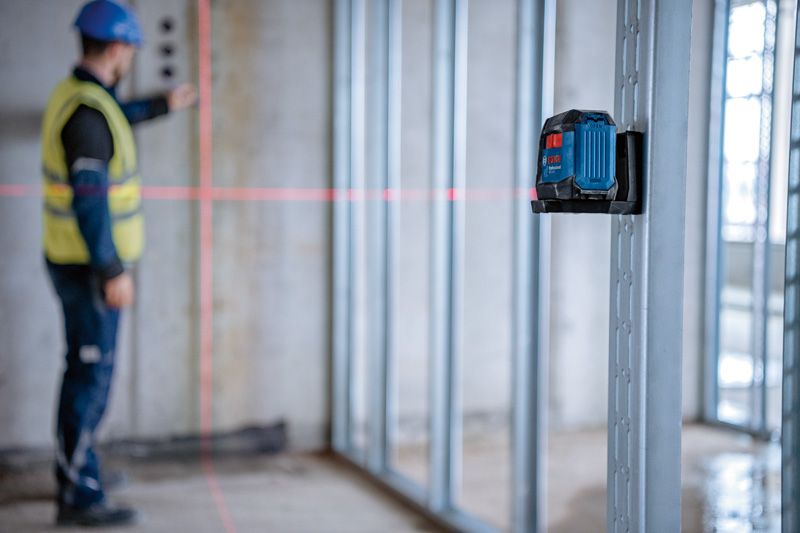 A person wearing safety equipment aligns wall studs using a laser leveling tool.
