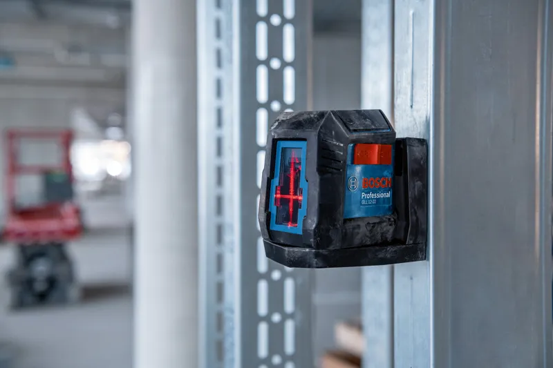 Laser leveling tool projecting red lines onto a metal frame in a construction area.