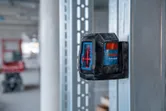 Laser leveling tool projecting red lines onto a metal frame in a construction area.