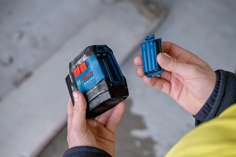A person holds a laser leveling tool and inserts a battery compartment.