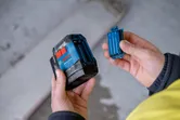 A person holds a laser leveling tool and inserts a battery compartment.
