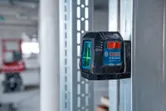Laser leveling tool projecting green lines onto a metal stud in a construction area.