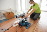 A person wearing safety equipment cuts laminate flooring with a miter saw.