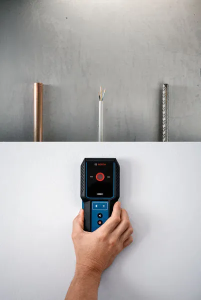 A person uses a detector to scan a wall for hidden pipes and wires.
