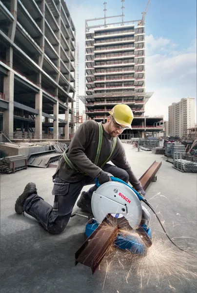 A person wearing safety equipment operates a metal cut-off saw, producing sparks on steel beams.