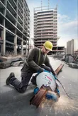 A person wearing safety equipment operates a metal cut-off saw, producing sparks on steel beams.