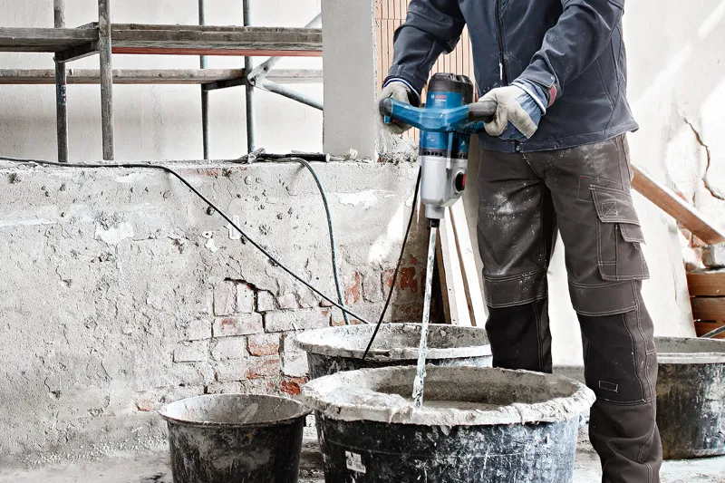 A person wearing safety equipment mixes construction material using a stirring mechanism.