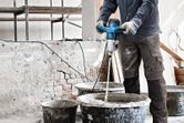 A person wearing safety equipment mixes construction material using a stirring mechanism.