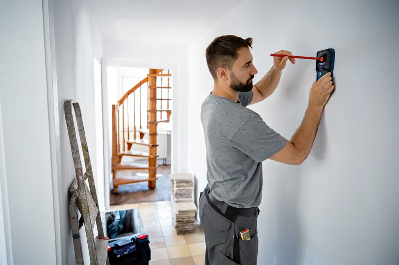 Person using a detector to mark a spot on a white wall.