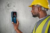 A person wearing safety equipment uses a detector on a concrete wall.