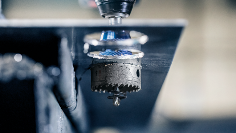 Hole saw attachment drilling through a sheet of metal.