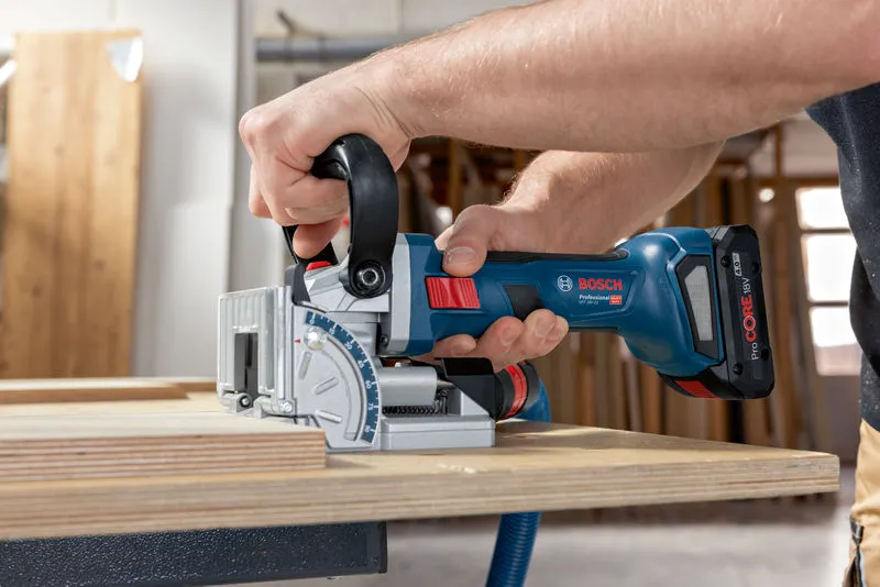 Person cuts plywood with a cordless biscuit joiner on a workbench.