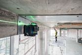 Laser leveling tool projects a green line across a concrete beam as a person wearing safety equipment works nearby.
