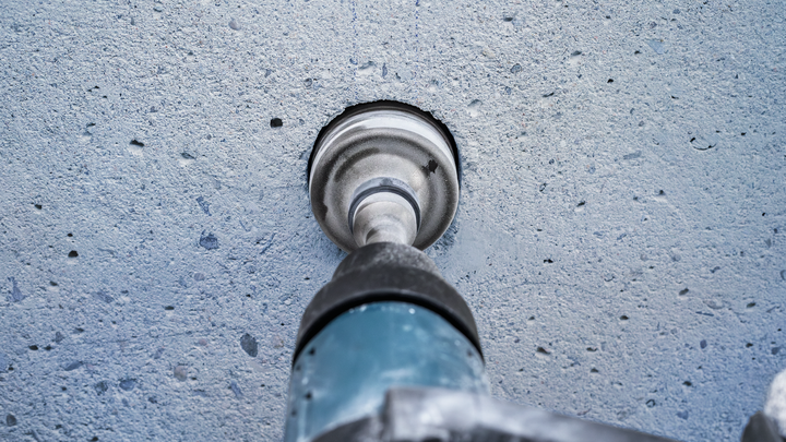 A rotary hammer drills a large hole into a concrete wall.