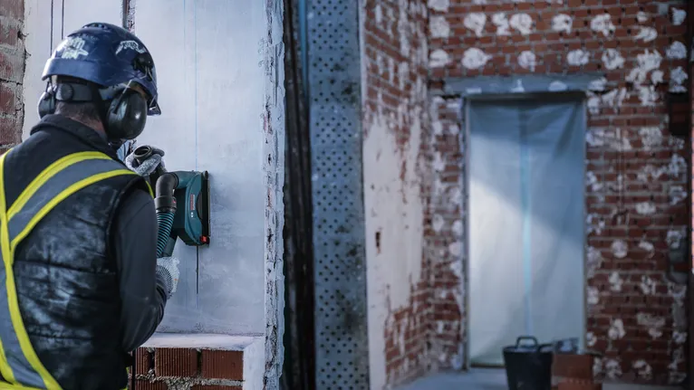 Person wearing safety equipment grinds a concrete wall at a construction site.