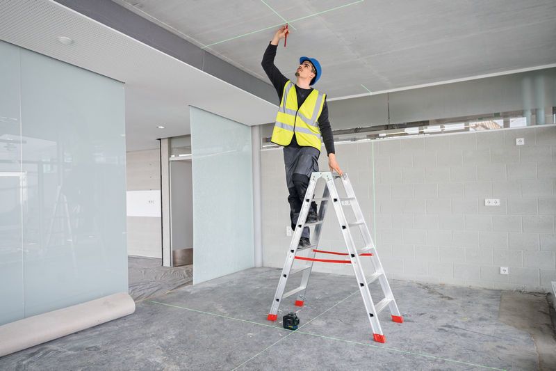 A person wearing safety equipment marks a ceiling using a laser leveling tool.