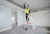 A person wearing safety equipment marks a ceiling using a laser leveling tool.