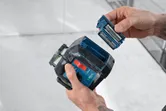A person inserts batteries into a laser leveling tool.