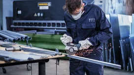 Person wearing safety equipment uses a cutting tool on a metal bar in a workshop.