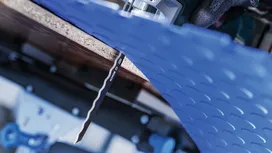 A person wearing safety equipment uses a jigsaw to cut through blue sheet material.