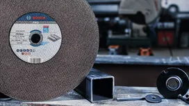 Large abrasive cutting disc next to metal pipe and metal parts on a workbench.