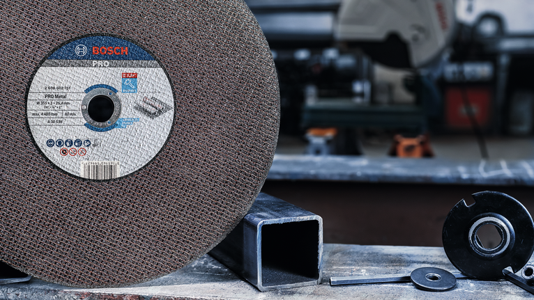 Large abrasive cutting disc next to metal pipe and metal parts on a workbench.