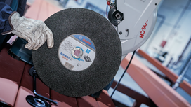 Person wearing safety equipment holds a large abrasive cutoff wheel near a metal saw.