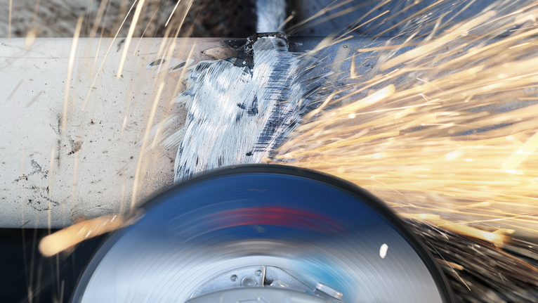 Angle grinder cutting through a metal pipe with bright sparks flying.